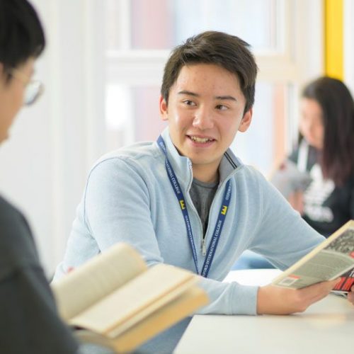 Student reading literary text and conversing with a fellow student